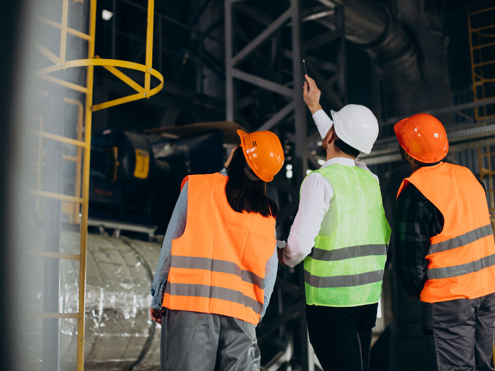 Personal con equipo de protección inspeccionando maquinaria industrial en planta sujeta a cumplimiento de la NOM-004-STPS